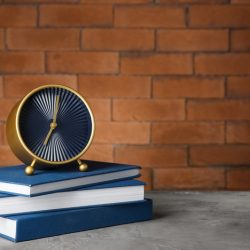 Alarm clock with books on table against brick background. Time management concept