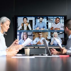 Global corporation online videoconference in meeting room with diverse people sitting in modern office and multicultural multiethnic colleagues on big screen monitor. Business technologies concept.